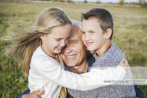 Smiling grandfather embracing grandchildren at field