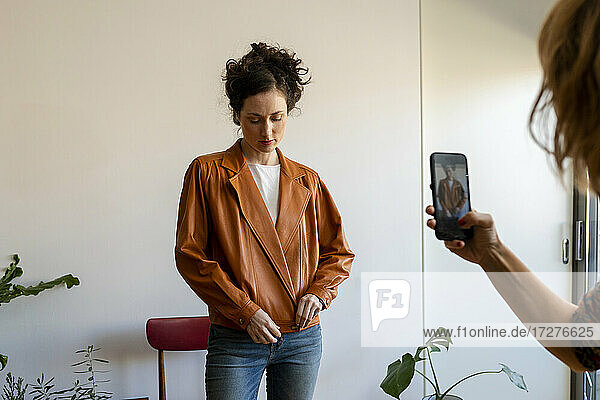 Eine Freundin fotografiert eine schöne Frau mit ihrem Smartphone  die zu Hause steht