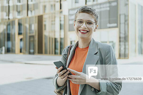 Mid erwachsene Frau lächelnd mit Smartphone auf der Straße in der Stadt stehend