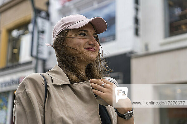 Junge Frau hält Einweg-Kaffeebecher  während sie auf der Straße in der Stadt steht
