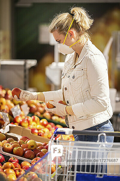 Jugendliches Mädchen mit Schutzmaske und Handschuhen beim Aussuchen von Äpfeln im Supermarkt