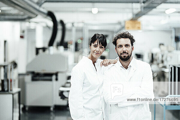 Männliche und weibliche Wissenschaftler in weißen Laborkitteln stehen vor einem hellen Labor