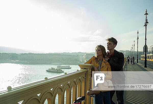 Nachdenkliches Paar  das am Geländer einer Brücke gegen den Himmel steht und wegschaut