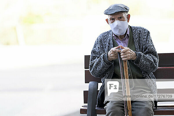 Älterer Mann mit Gesichtsschutzmaske sitzt auf einer Bank im Freien