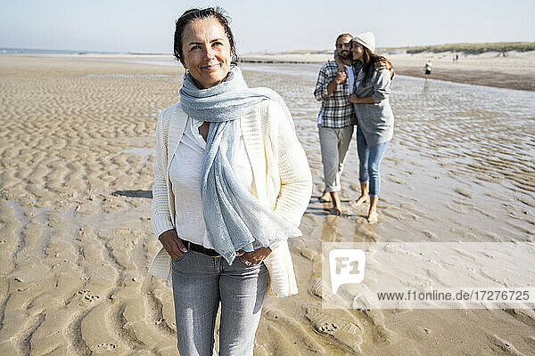 Mature woman looking away while standing with couple in background at beach