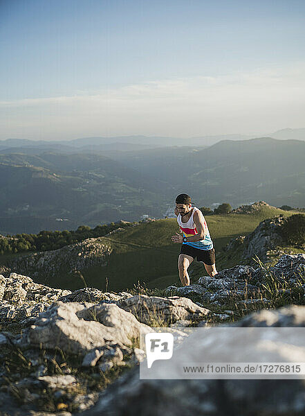 Mann läuft auf Bergpfad gegen Gebirge und klaren Himmel