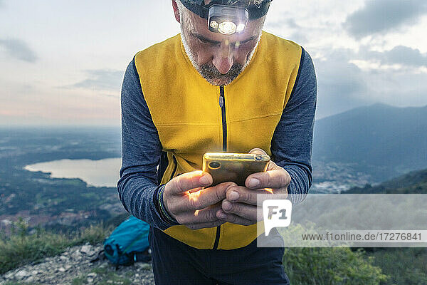 Mature male hiker using smart phone while standing against sky at sunset