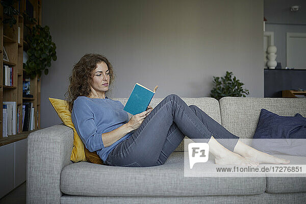 Woman reading book while sitting on sofa at home
