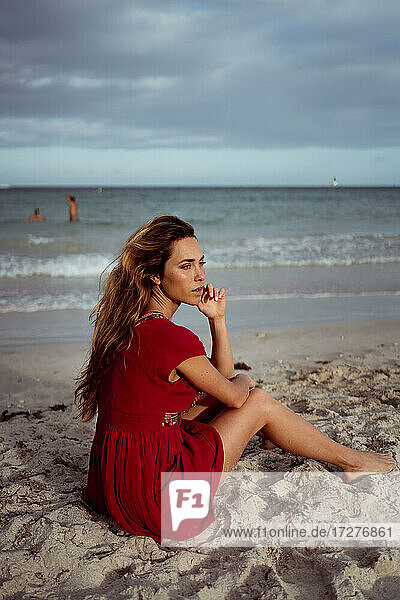 Nachdenkliche Frau  die wegschaut  während sie am Ufer des Strandes sitzt