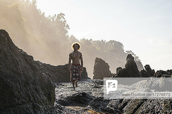 Junger Mann  der auf einer Felsformation am Strand gegen den Himmel läuft