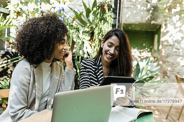 Geschäftsfrau betrachtet eine Kollegin  die ein digitales Tablet benutzt  im Café sitzend