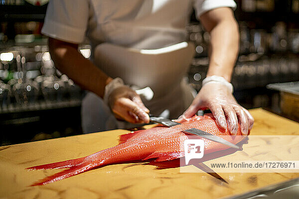 Koch schneidet Fisch auf einem Schneidebrett in einer Großküche eines Restaurants