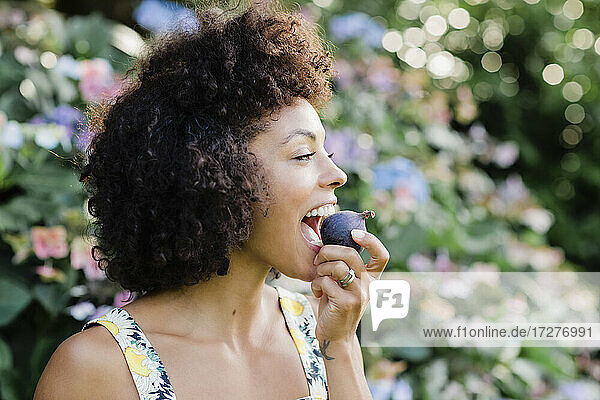 MId adult woman eating figwhile standing in front of flowering plant at park