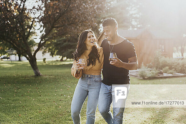 Happy man and woman with wineglass walking at backyard
