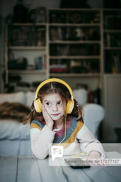 Girl wearing headphones looking away while leaning on table at home