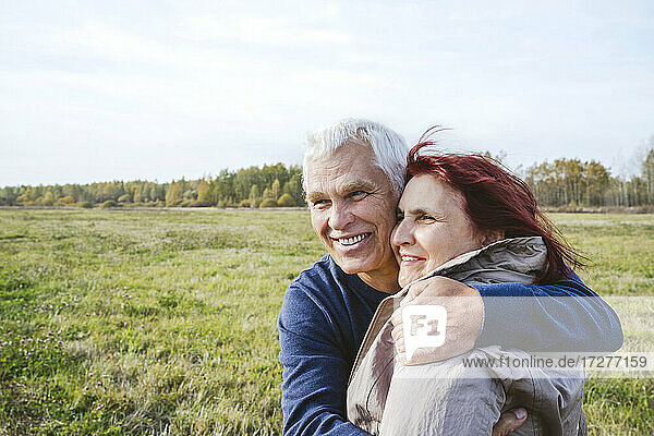 Glückliches älteres Paar  das sich umarmt  während es auf dem Feld wegschaut