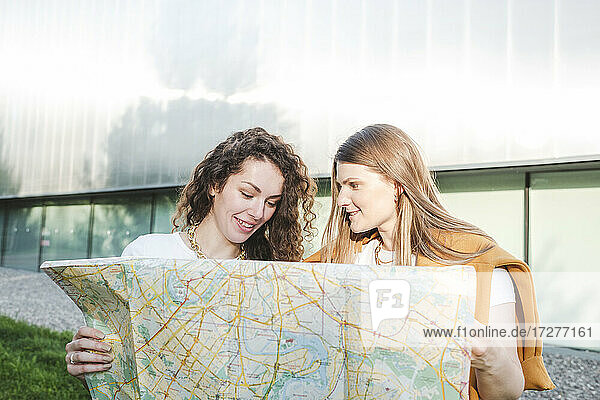 Lächelnde Freundinnen mit Stadtplan in der Hand an einem sonnigen Tag