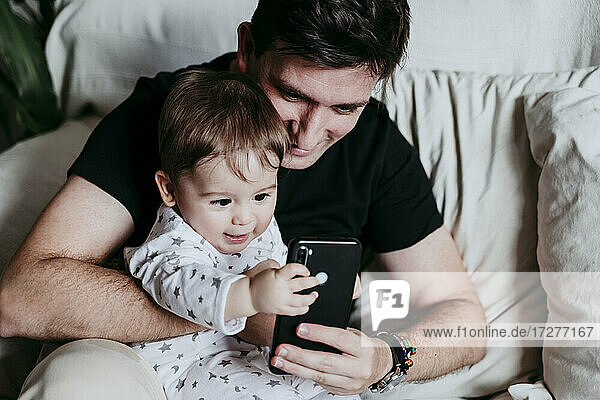 Vater und Sohn benutzen ein Smartphone  während sie zu Hause auf dem Sofa sitzen