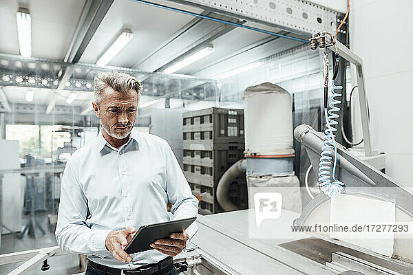 Mature businessman using digital tablet while standing by machinery in industry