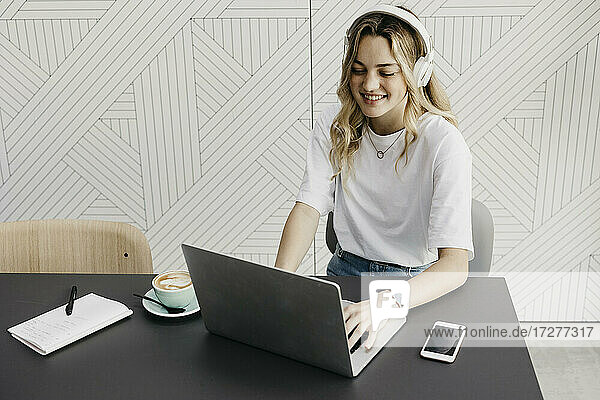 Lächelnde Frau mit Kopfhörern  die an einem Laptop in einem Café arbeitet
