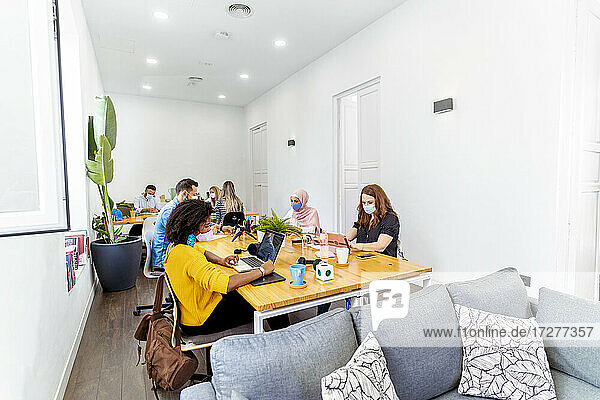 Geschäftsleute mit Gesichtsmaske  die in sozialer Distanz sitzen  während sie im Büro sitzen