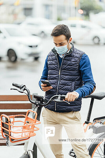 Junger Mann mit Fahrrad  der sein Smartphone benutzt  während er auf der Straße steht