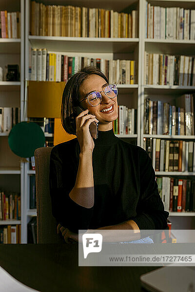 Lächelnde Geschäftsfrau  die mit ihrem Smartphone telefoniert und zu Hause sitzt