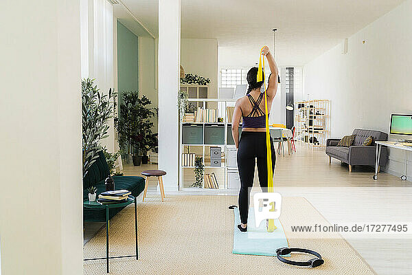 Young woman stretching with resistance band standing at home