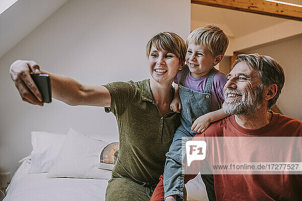 Glückliche Mutter  die ein Selfie mit ihrem Smartphone macht  während Vater und Sohn daneben sitzen