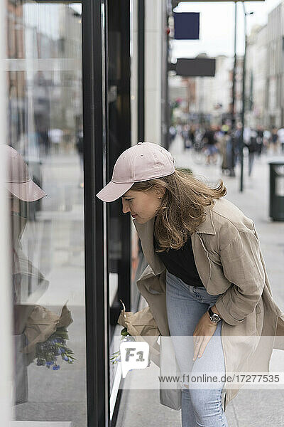 Young woman looking at glass door while standing on footpath