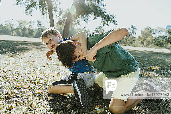 Smiling brothers embracing each other in public park on sunny day