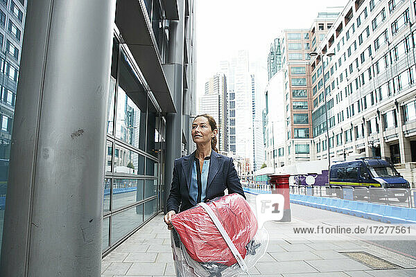 Lächelnd Geschäftsfrau hält Einkaufen Kleidung beim Gehen auf der Straße in der Stadt