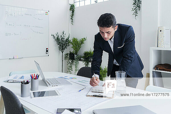 Gutaussehender Unternehmer schreibt in sein Tagebuch  während er am Schreibtisch eine Strategie plant