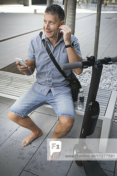 Mature man listening music through earphone while sitting on bench