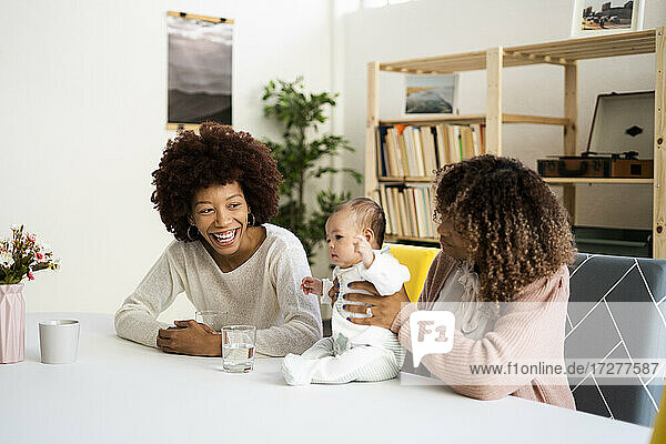 Mother with cute daughter by happy aunt at table in living room