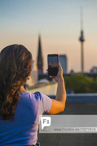 Frau  die auf dem Dach stehend mit ihrem Smartphone fotografiert