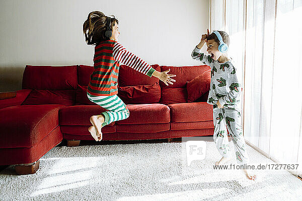 Männliche und weibliche Geschwister tragen Kopfhörer  während sie gegen das Sofa im Wohnzimmer tanzen