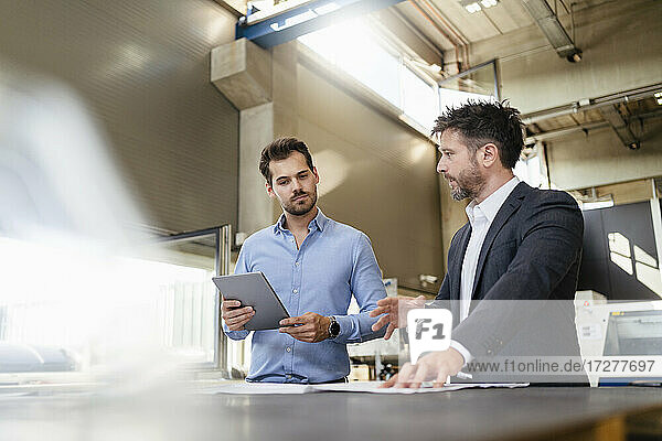 Geschäftsmann im Gespräch mit einem Kollegen  der ein digitales Tablet hält  während er in einer Fabrik steht