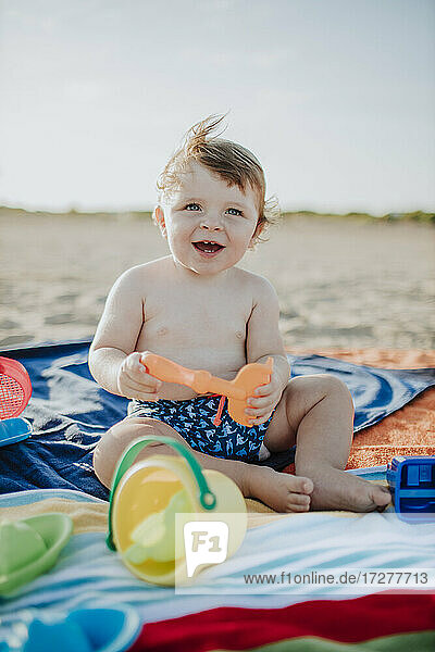 Süßes Baby Junge spielt mit Spielzeug am Strand bei Sonnenuntergang