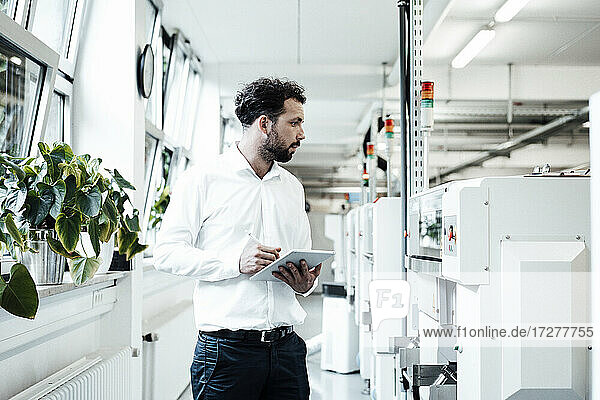Geschäftsmann hält ein digitales Tablet in der Hand  während er sich Maschinen in der hellen Industrie ansieht