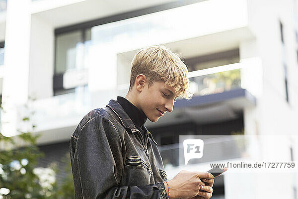 Blonder Teenager mit Smartphone in der Stadt