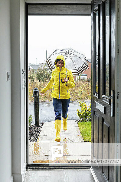 Frau läuft mit Regenschirm zu Hause während der Regenzeit