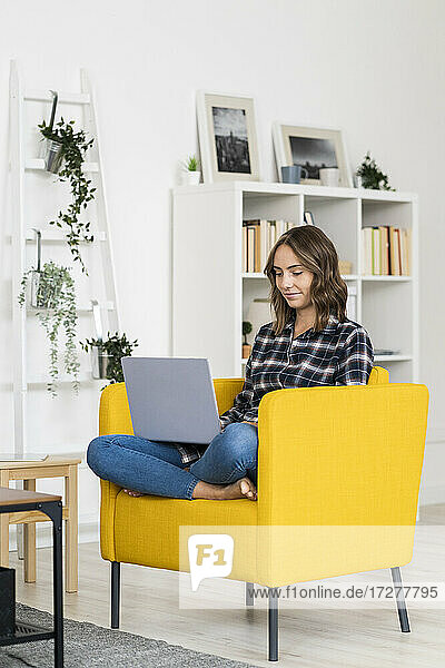 Junge Frau benutzt einen Laptop  während sie zu Hause auf dem Sofa sitzt