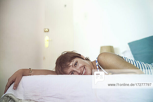 Lächelnde junge Frau auf dem Bett liegend zu Hause
