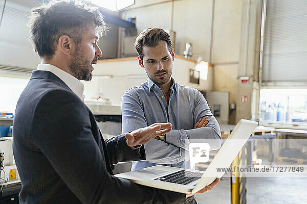 Mature man using laptop while standing by colleague at factory