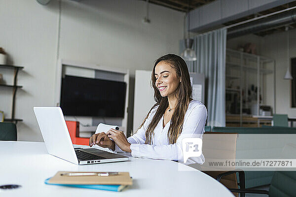 Smiling businesswoman using latptop at desk in office