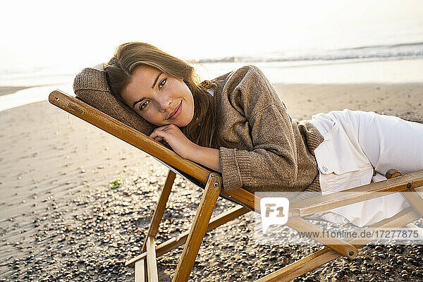 Schöne junge Frau  die sich auf einem Klappstuhl am Strand bei Sonnenuntergang entspannt