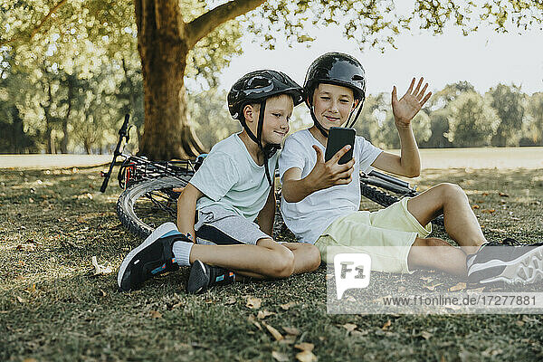 Brothers doing video call on smart phone sitting in public park