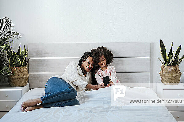 Mutter und Tochter benutzen ein Smartphone auf dem Bett im Schlafzimmer zu Hause
