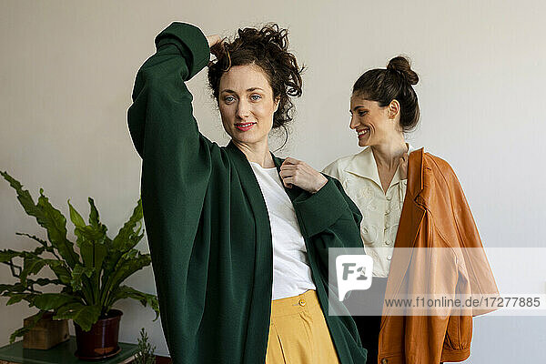 Beautiful woman with hand in hair standing with smiling female model at home
